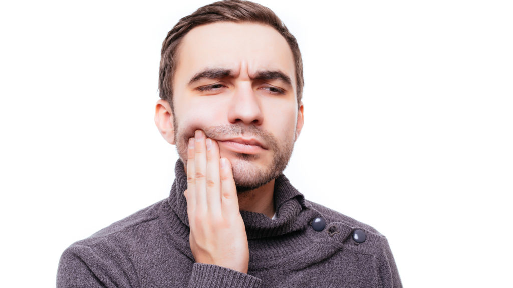 Young man holding the side of his face while waiting to see the dentist about a dental crown