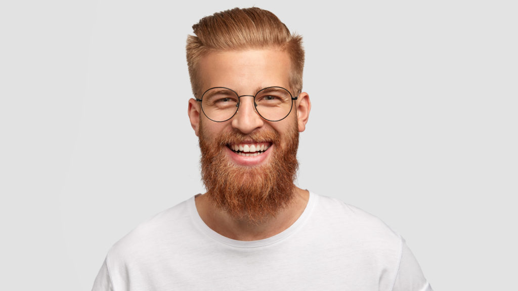 Young male with glasses and beard smiling after getting veneers.