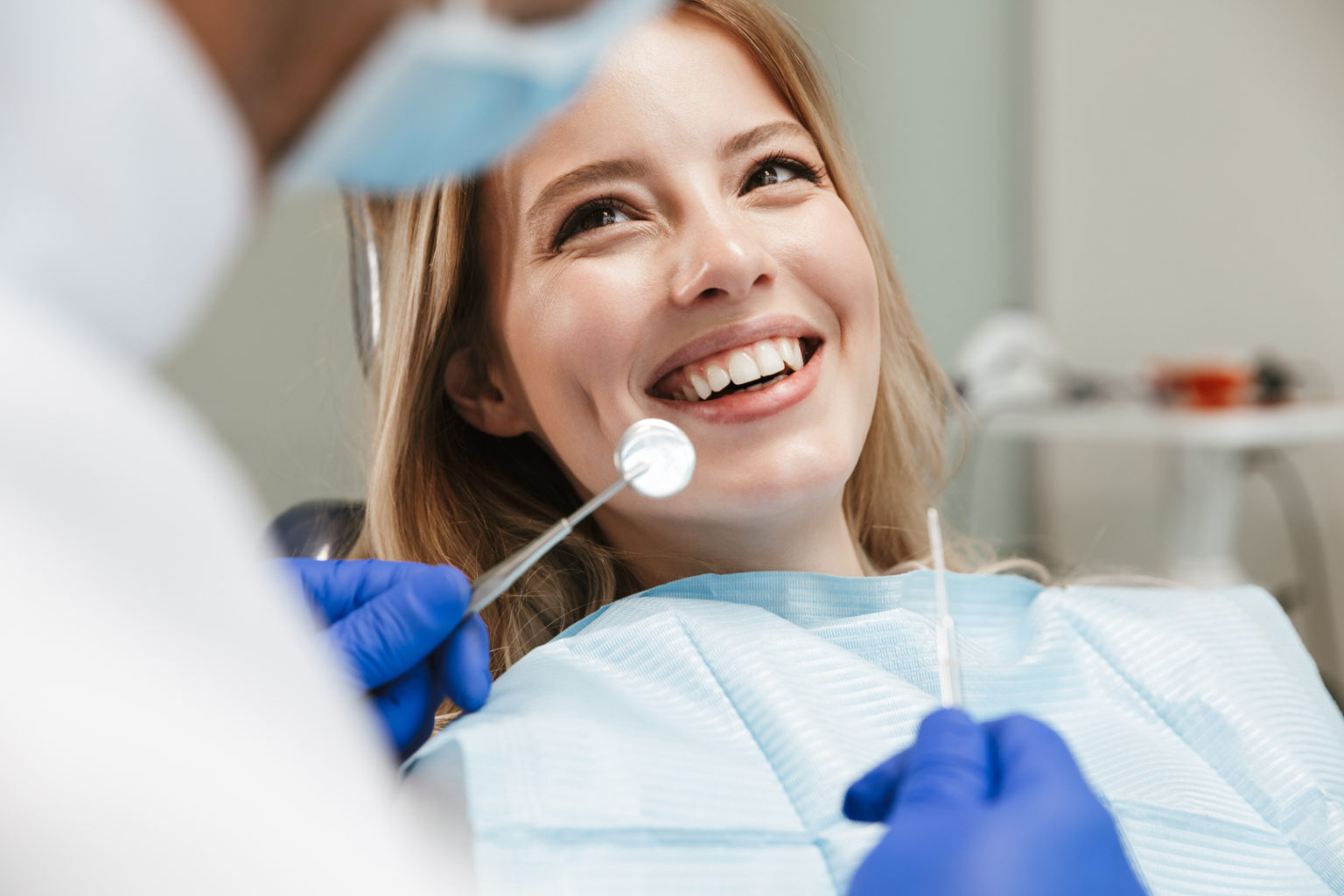 Image of pretty young woman sitting in dental chair at medical center while professional doctor fixing her teeth with veneers
