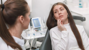 Young woman holding her cheek as she waits to see the emergency dentist.