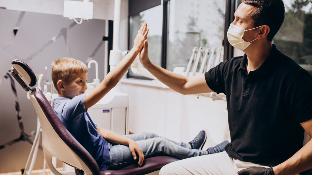 Dentist and young boy in dentist chair high fiving after the young boy came to see an emergency dentist Beverly Hills.