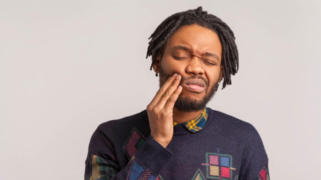 Image of young man holding his cheek and grimacing from gum disease pain.