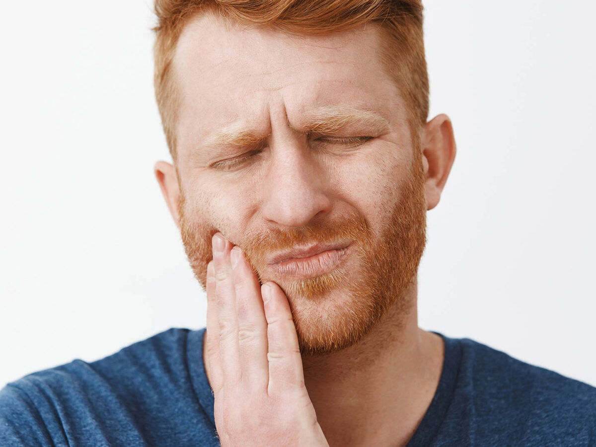 Man holding cheek suffering from dental pain, wondering when to visit a dentist.