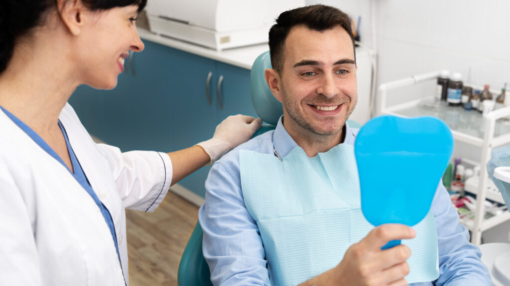Male patient holding up mirror and looking at his professional dental cleaning.