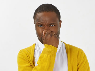 Man in yellow sweater holding his nose and wondering how to cure bad breath permanently.