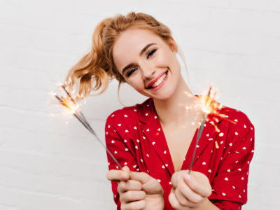 Woman in red dress holding sparklers and asking about everyone's New Year's Resolutions: Dental Health Edition